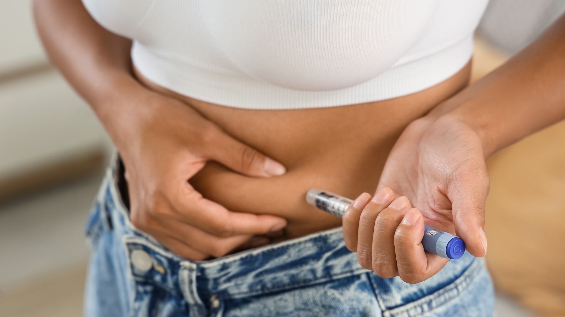 Person holding a glucose meter to their lower abdomen while another hand steadies the skin, suggesting a diabetes check.