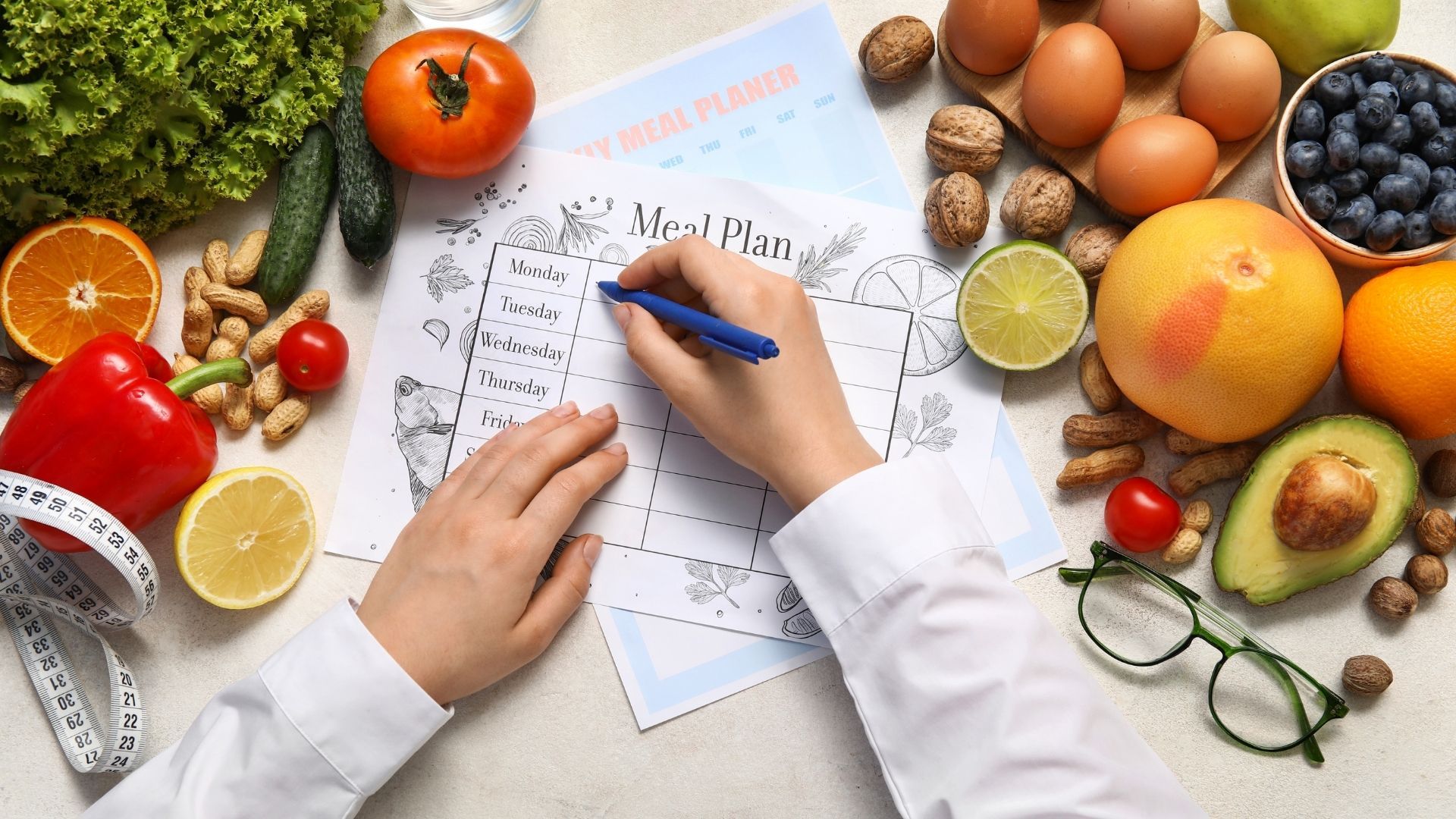 Hands writing a meal plan beside fresh fruits, eggs, and vegetables on a kitchen counter
