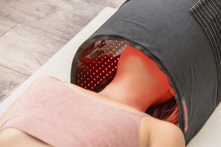 Close-up of a person using a red infrared light therapy device on their neck and shoulder