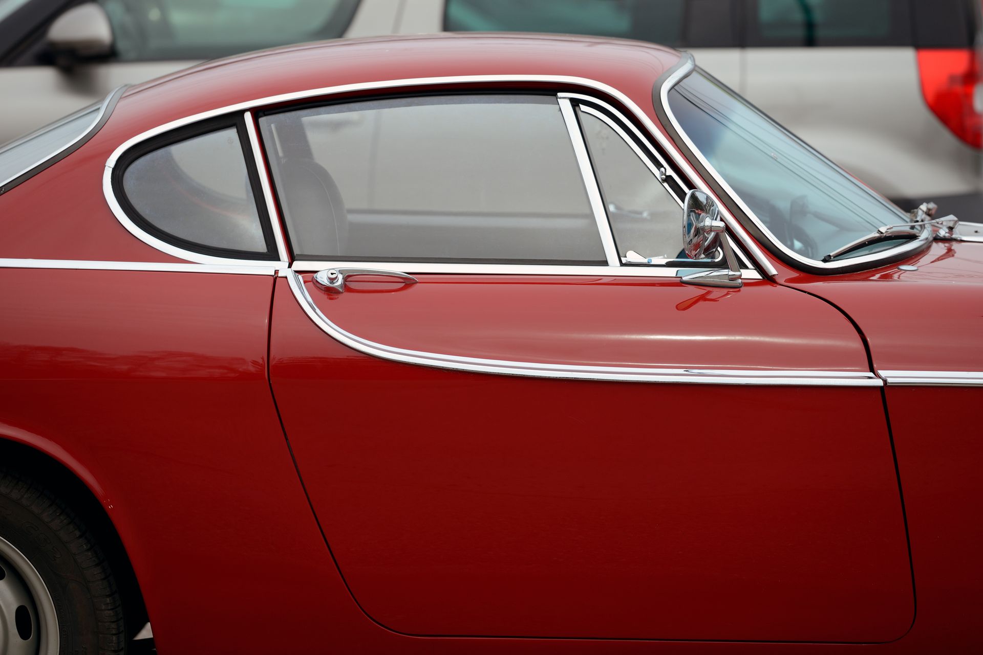 Close-up of a classic red car's side window and chrome door trim. Close-up of a classic red car's side window and chrome door trim.