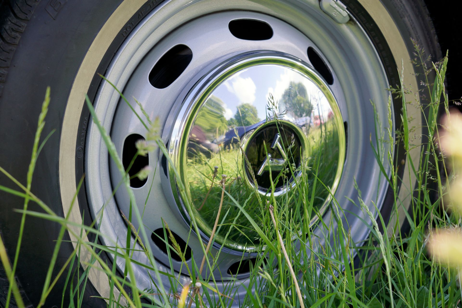 Close-up of a chrome car wheel rim surrounded by tall grass.