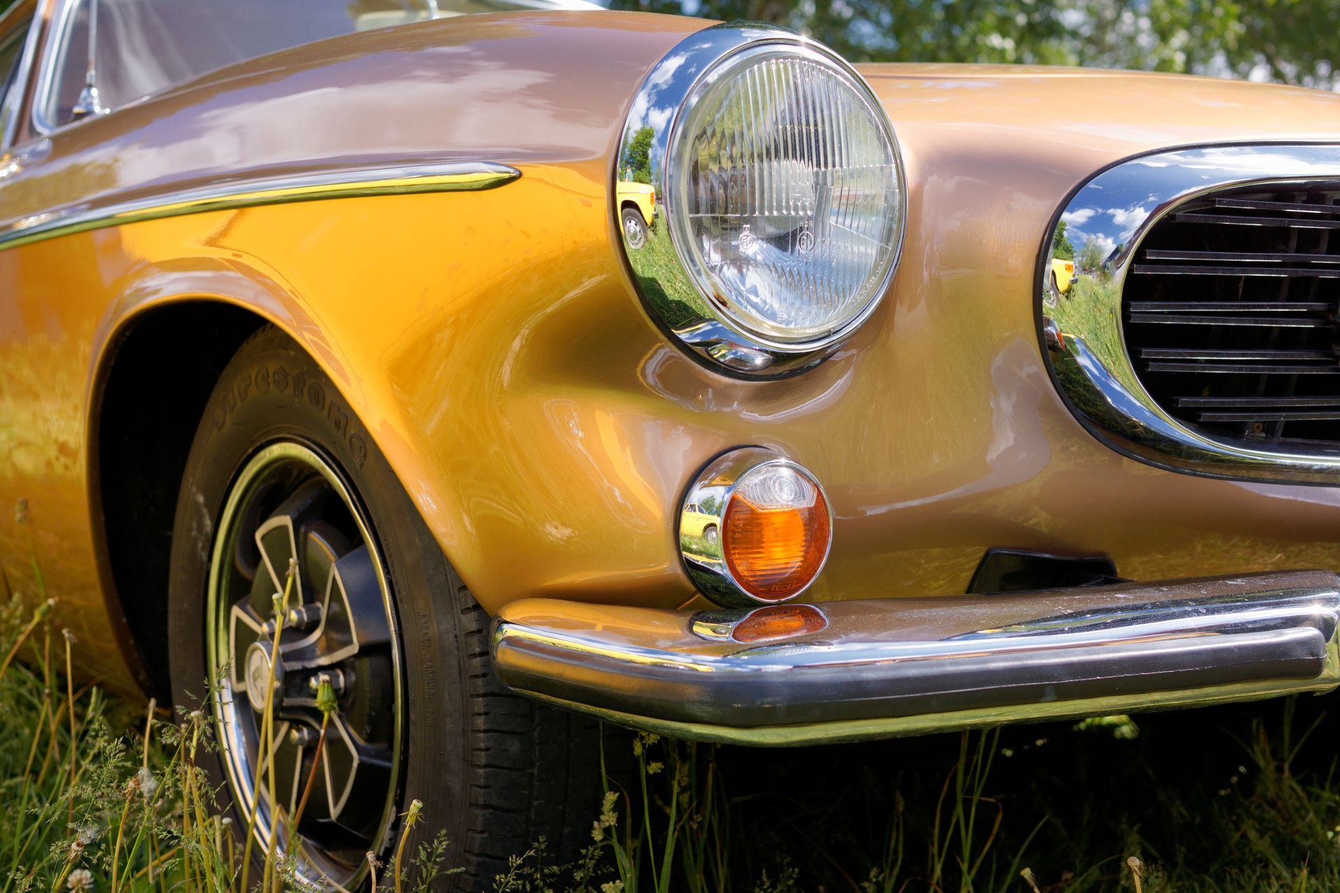 Close-up of a classic Volvo's headlight, grille, and front fender.