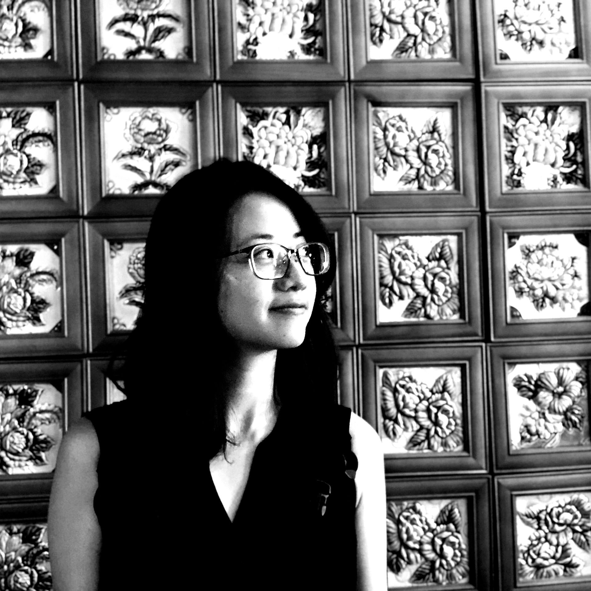 一個戴著眼鏡的女人站在牆上，牆上掛著花。