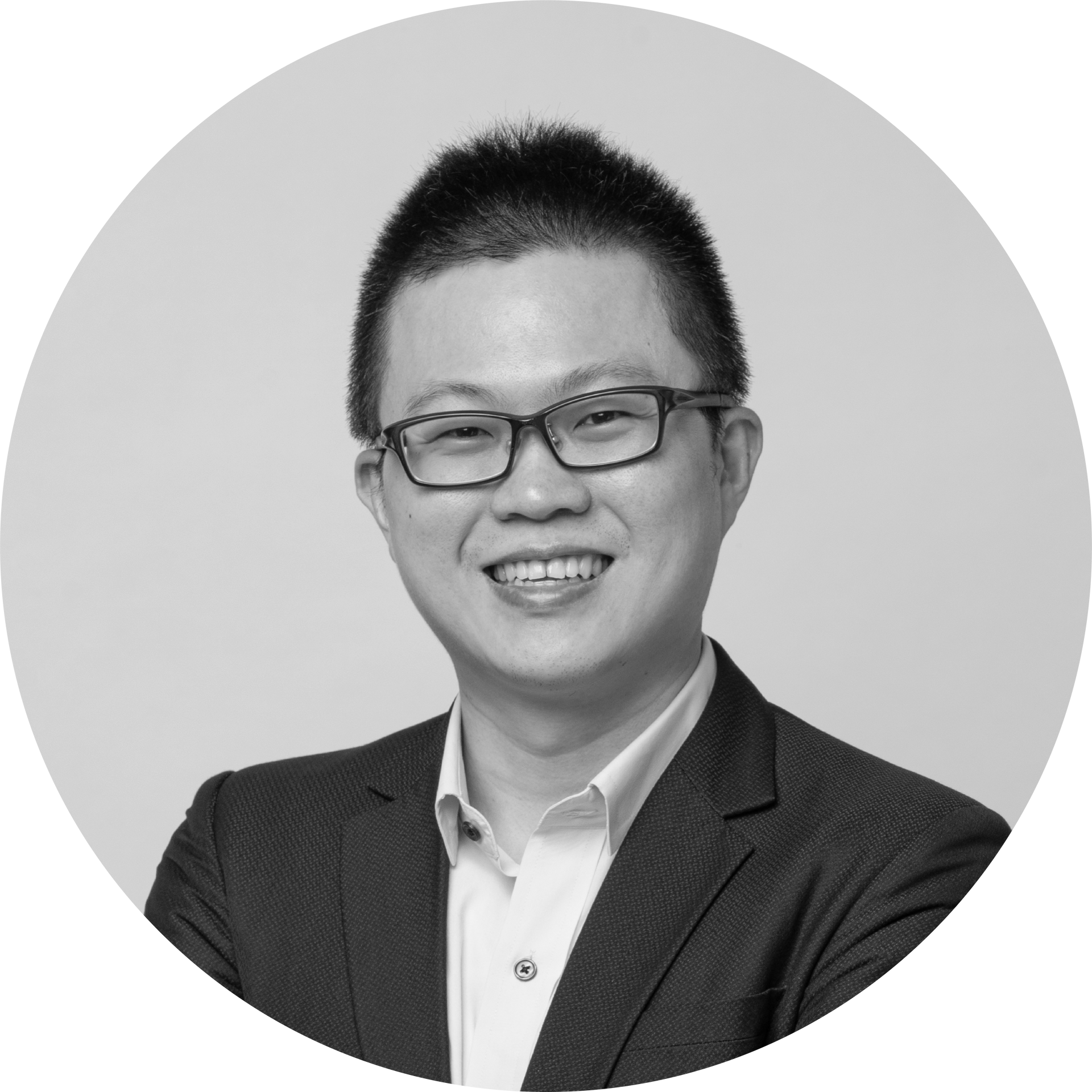 黑白照片中，一個穿著西裝、戴眼鏡的男人微笑著。
