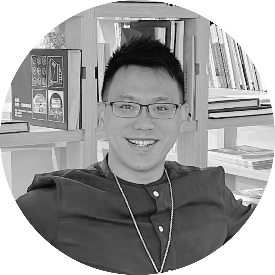 一個戴著眼鏡、戴著項鍊的男人在書架前微笑。