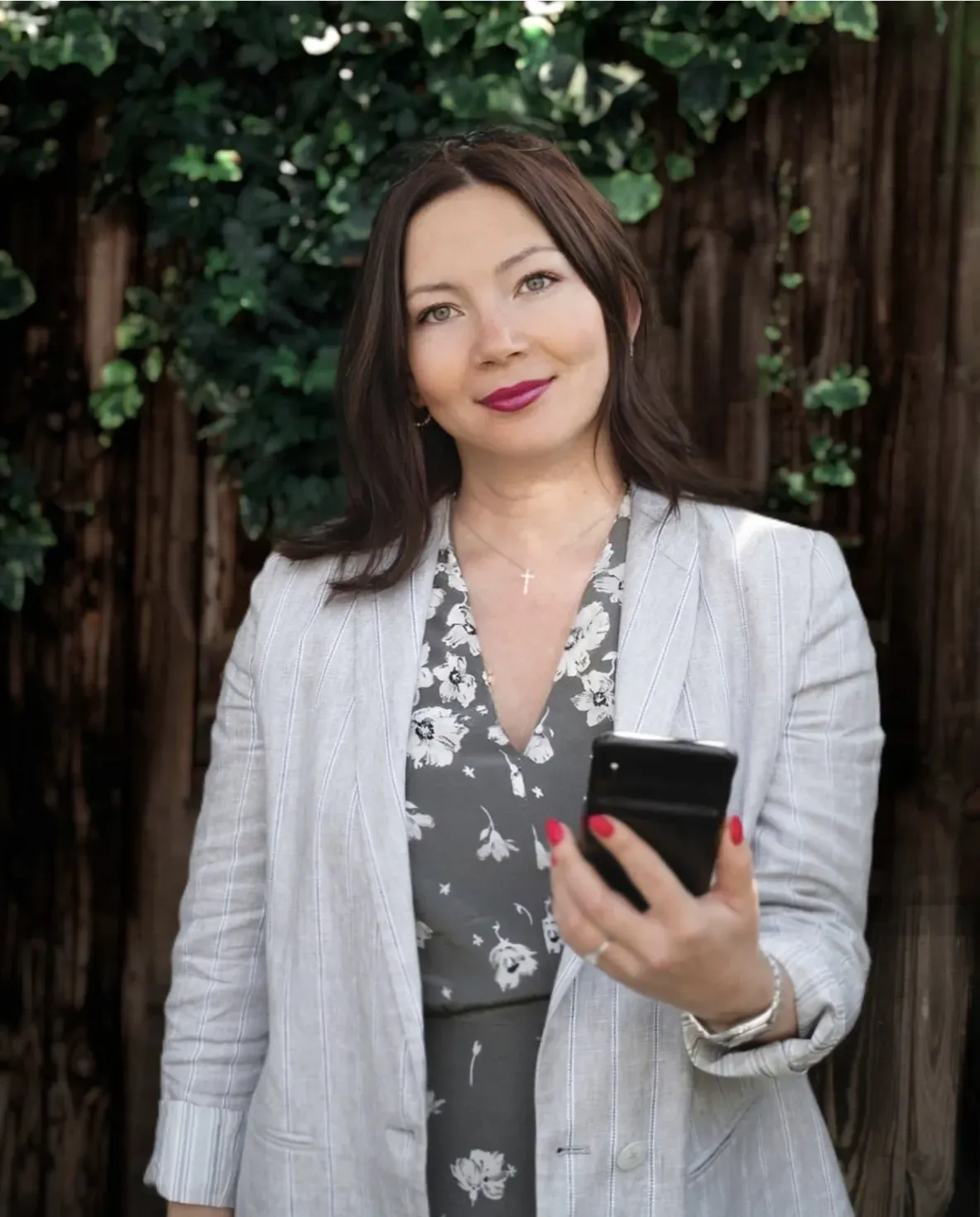 A woman is standing in front of a wooden fence holding a cell phone.