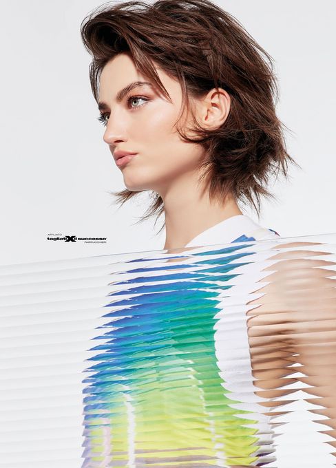 Ritratto di profilo di una persona con capelli castani corti che indossa una maglietta a righe colorate, su sfondo bianco.