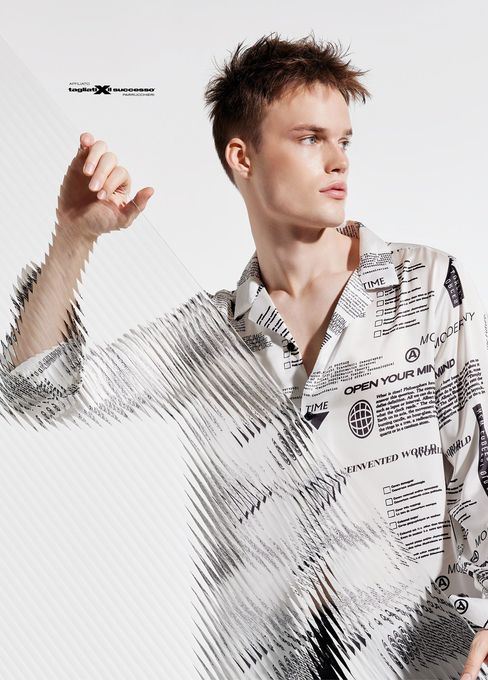 Giovane uomo con una camicia bianca a fantasia che guarda di lato su uno sfondo chiaro