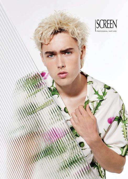 Ritratto di una modello bionda con una camicia bianca a fiori, in posa su uno sfondo bianco con strisce diagonali verdi.