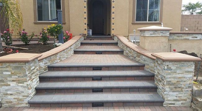 A set of tiered, brick-paved front steps leading to a house entrance, flanked by stone-veneer pillars and low walls.
