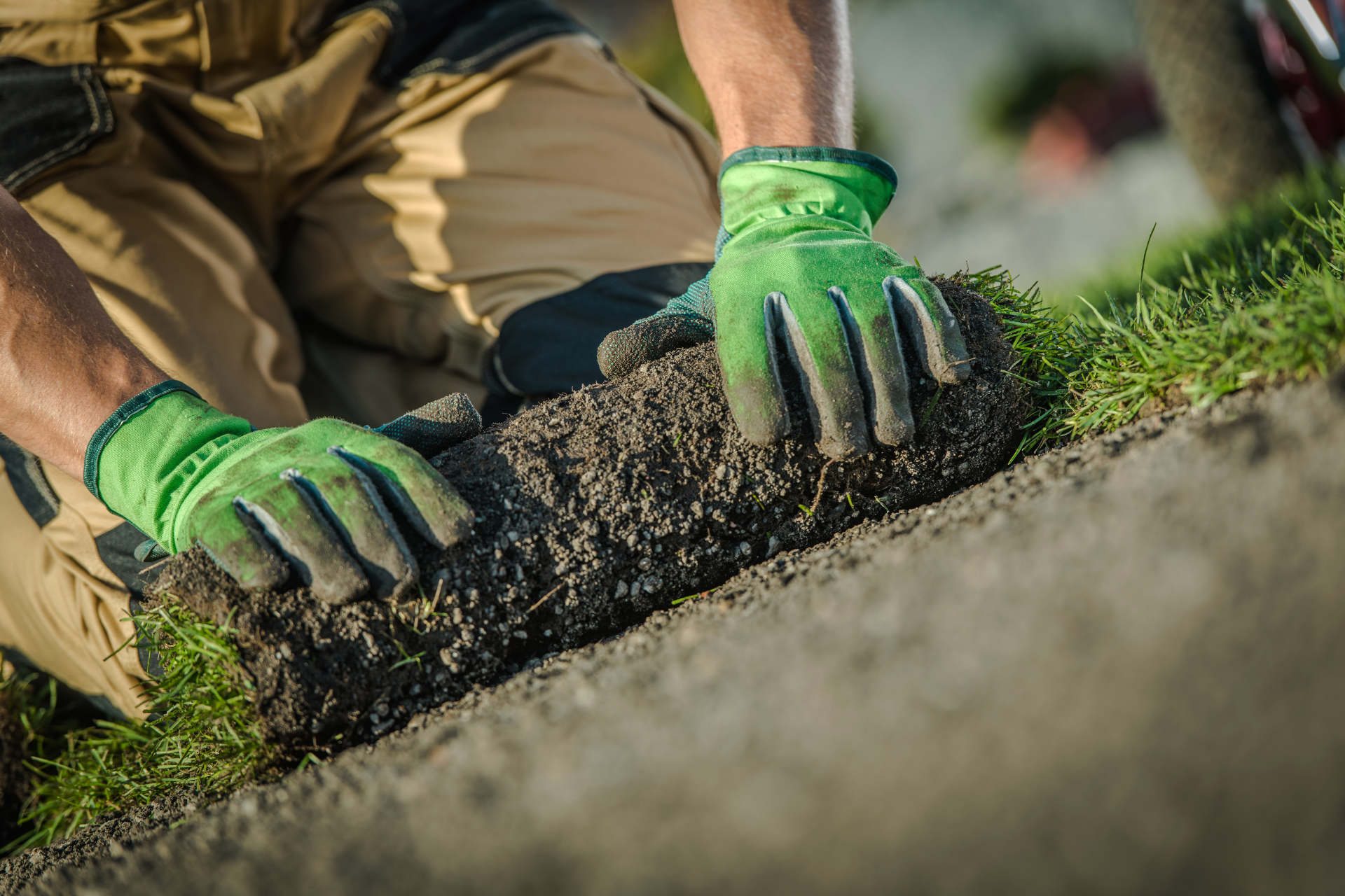 Gloved hands planting grass sod along a soil edge outdoors