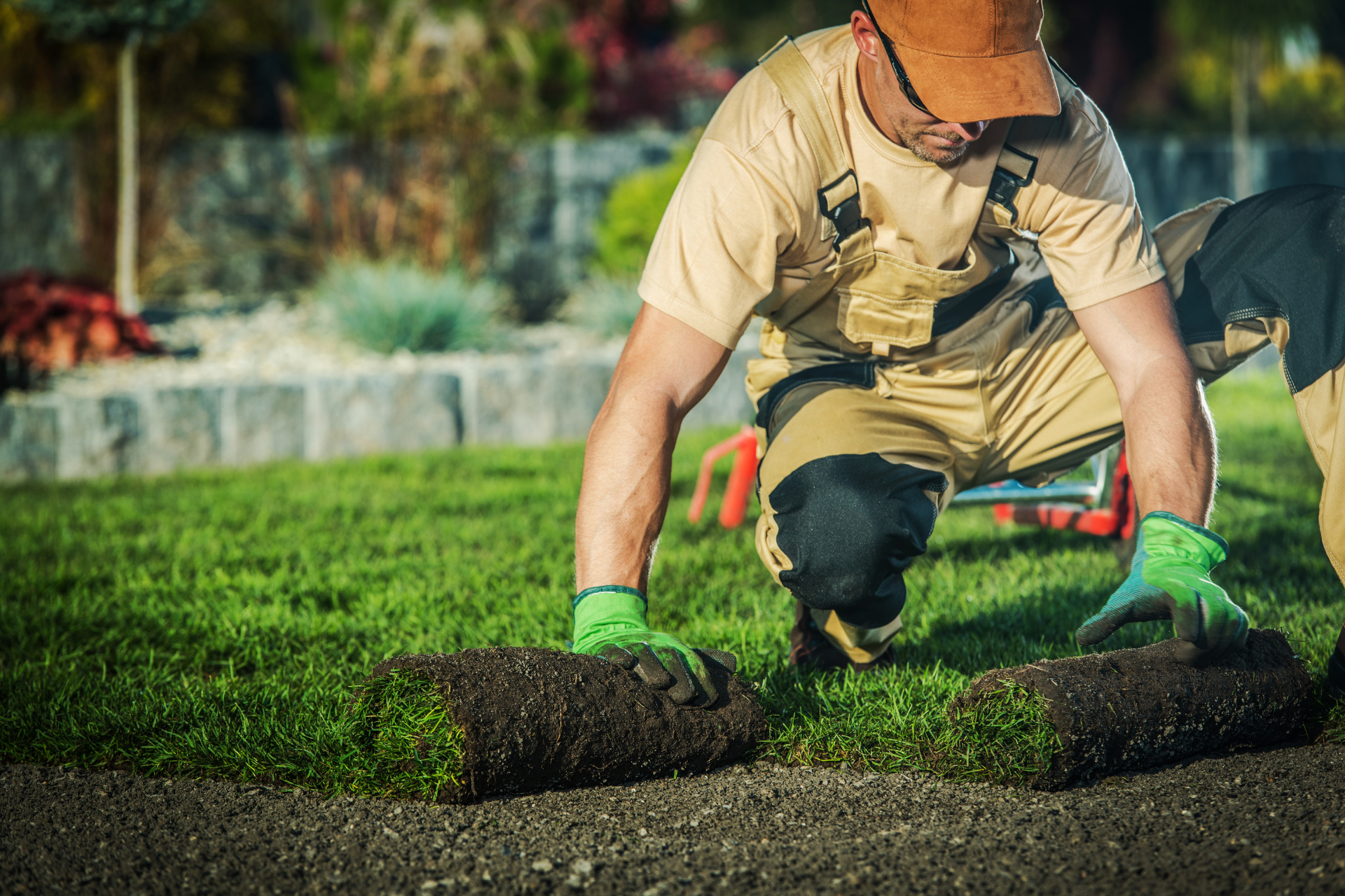 Worker laying sod in a garden, placing fresh grass beside a paved path.