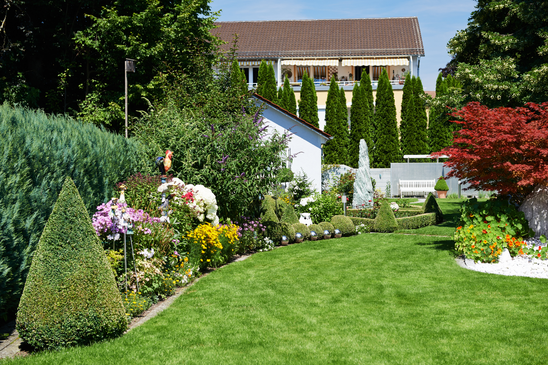 Lush garden with manicured lawn, colorful flowers, shrubs, and a house in the background