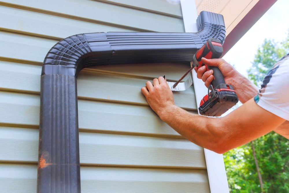 Person installing black gutter on house exterior with a drill