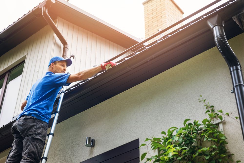 Worker cleaning gutters on a house with a ladder and roofline outstretched by a gutter vacuum tool
