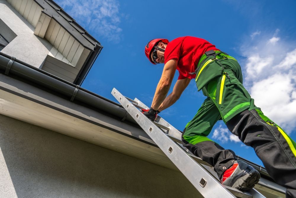 Worker on a ladder cleaning a house gutter under a cloudy sky