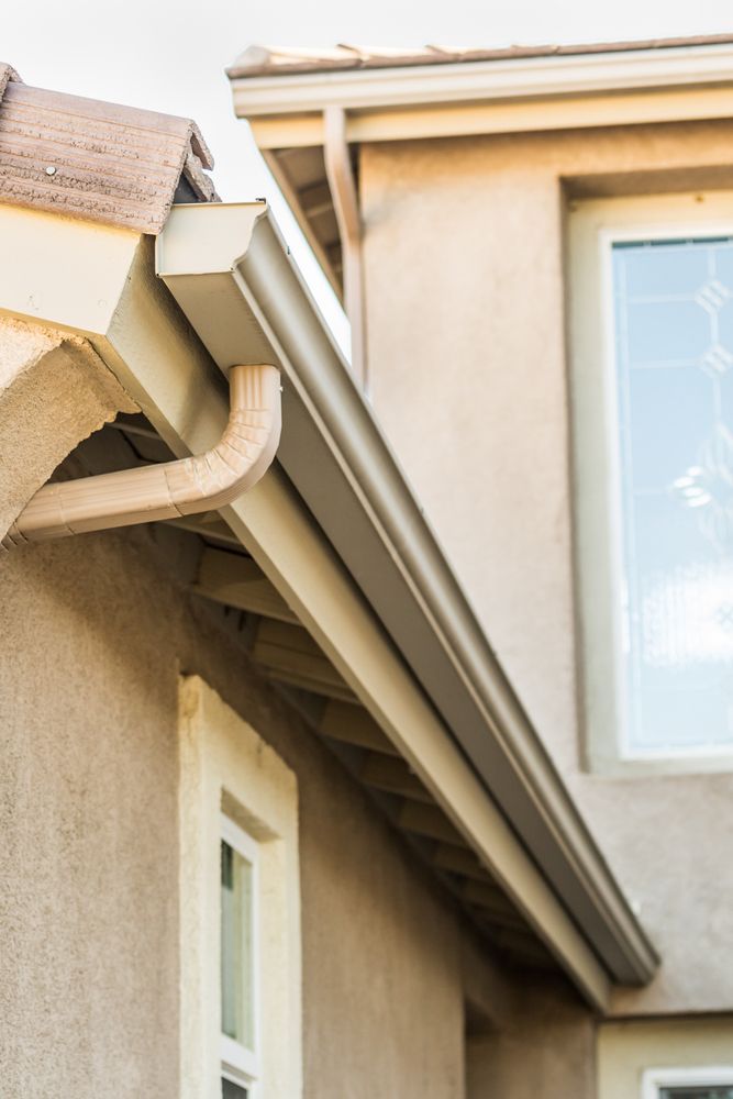 House roof eaves and guttering beside a beige exterior wall and window