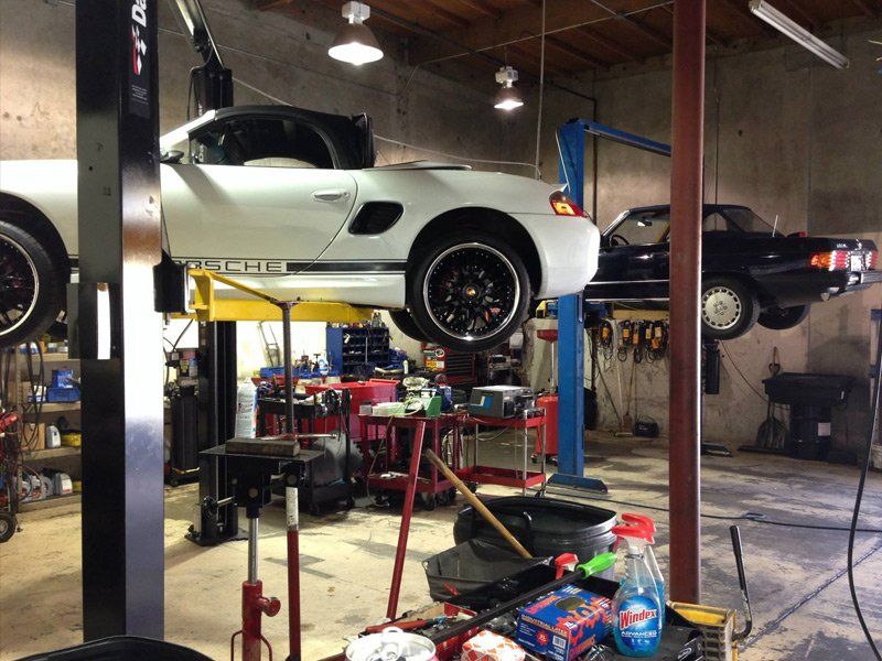 Two cars lifted on hydraulic lifts in an auto repair shop with tools and equipment below