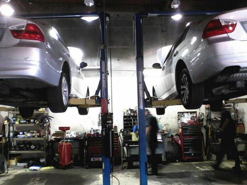 Two silver cars lifted on auto shop hoists in a garage