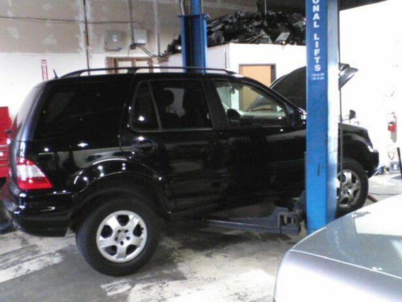 Black SUV on a car lift in an auto shop, with a blue pickup partially visible nearby