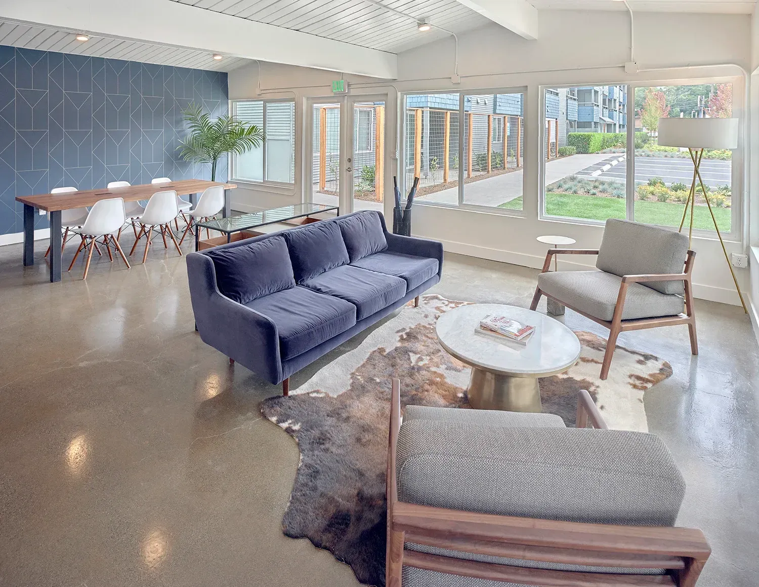 Modern lounge with a blue sofa, armchairs, a coffee table on a cowhide rug, and a dining table in a bright, open space.
