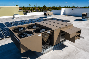 Outdoor rooftop HVAC units beside solar panels on a flat white roof under a clear sky
