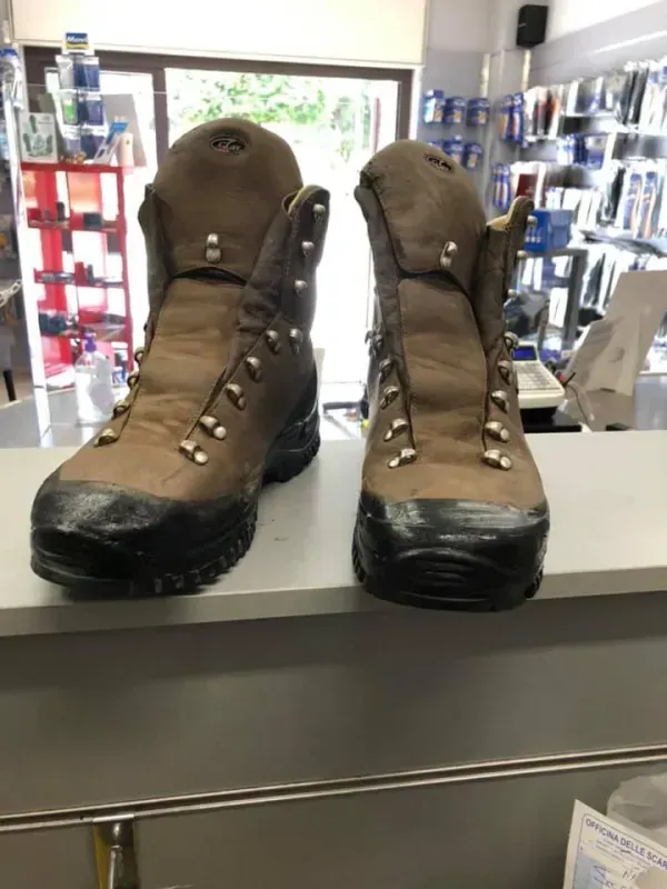 Scarponi da trekking marroni sul bancone di un negozio, con scaffali di calzature sullo sfondo.