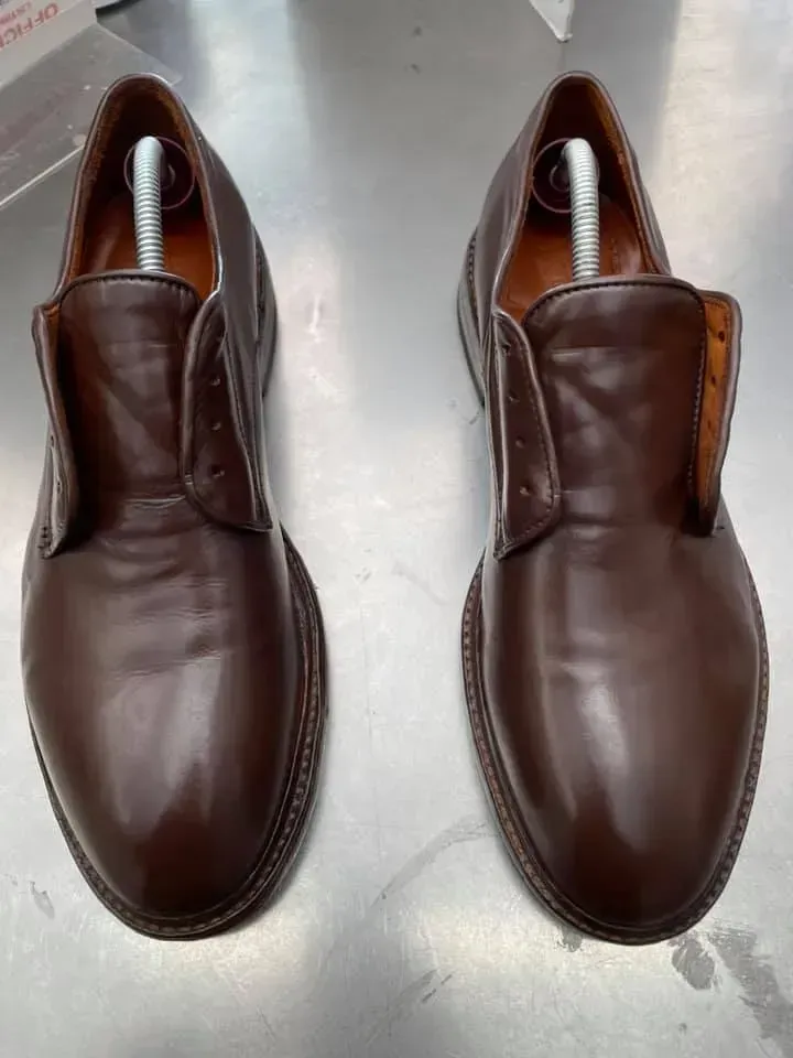 Un paio di scarpe mocassino in pelle marrone viste dall'alto su un pavimento grigio chiaro.