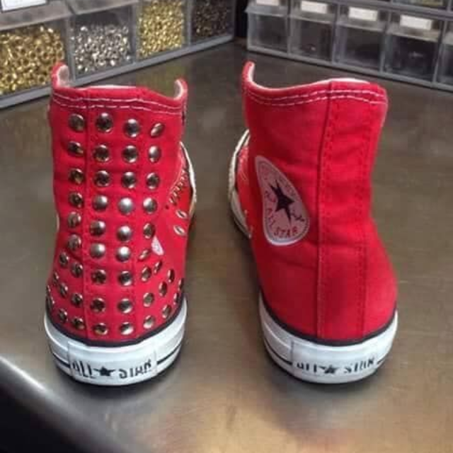 Un paio di scarpe da ginnastica rosse alte, una delle quali con borchie argentate, su uno scaffale di un negozio.