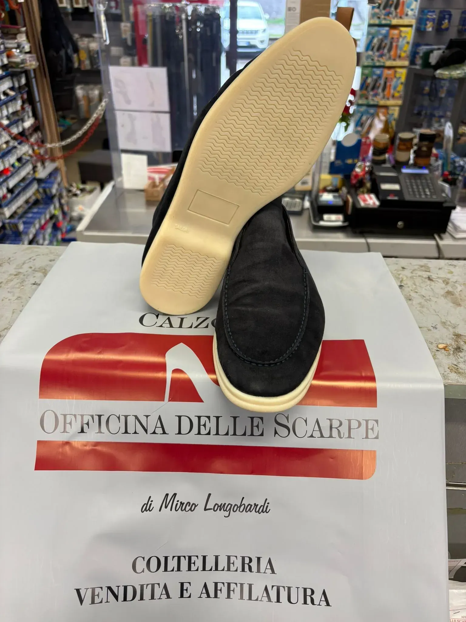 Una scarpa da ginnastica nera con suola beige è esposta su un espositore in negozio, sopra un cartello di saldi.