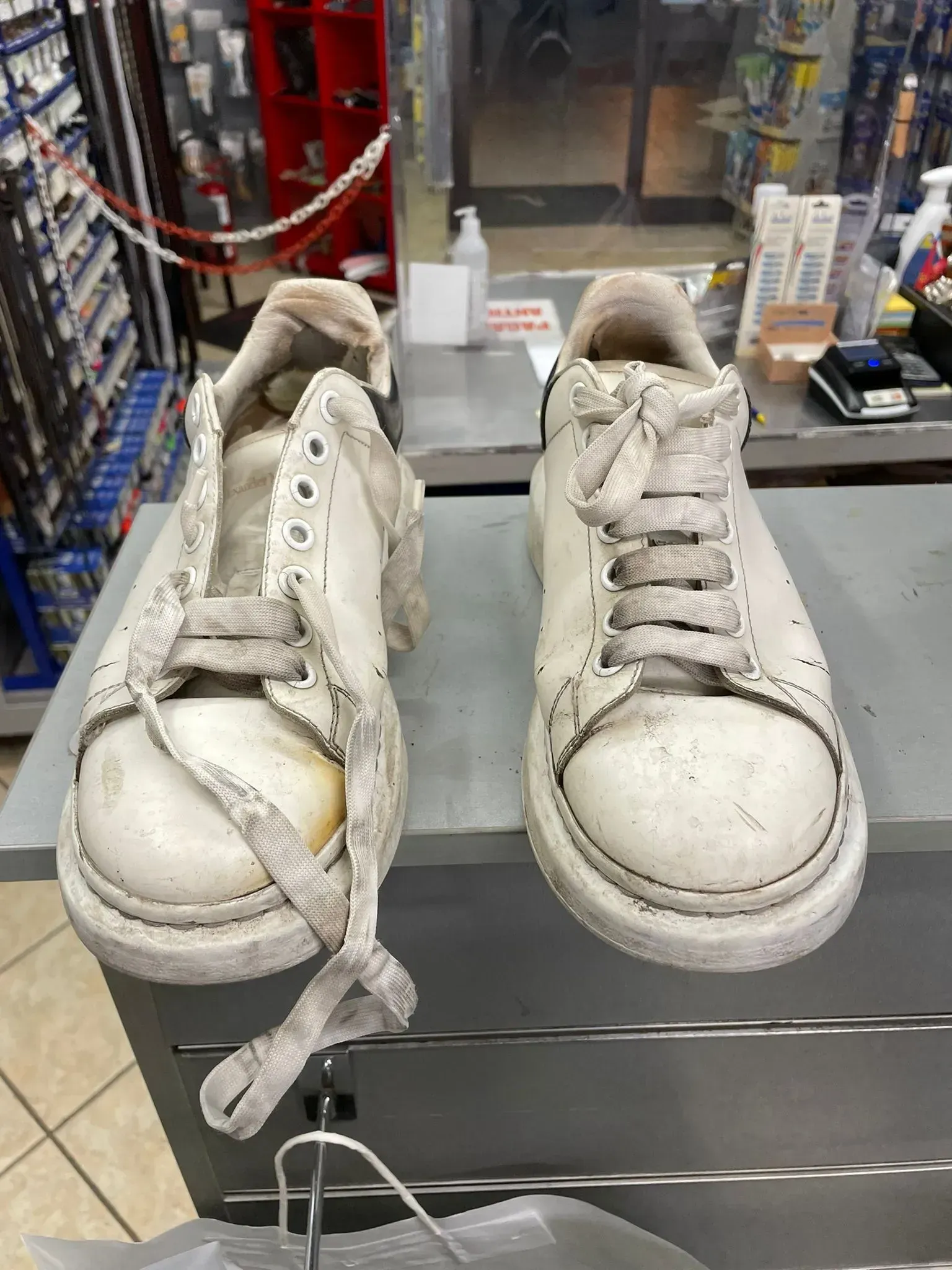 Scarpe da ginnastica bianche usurate, con lacci sfilacciati e punte graffiate, esposte sul bancone di un negozio.