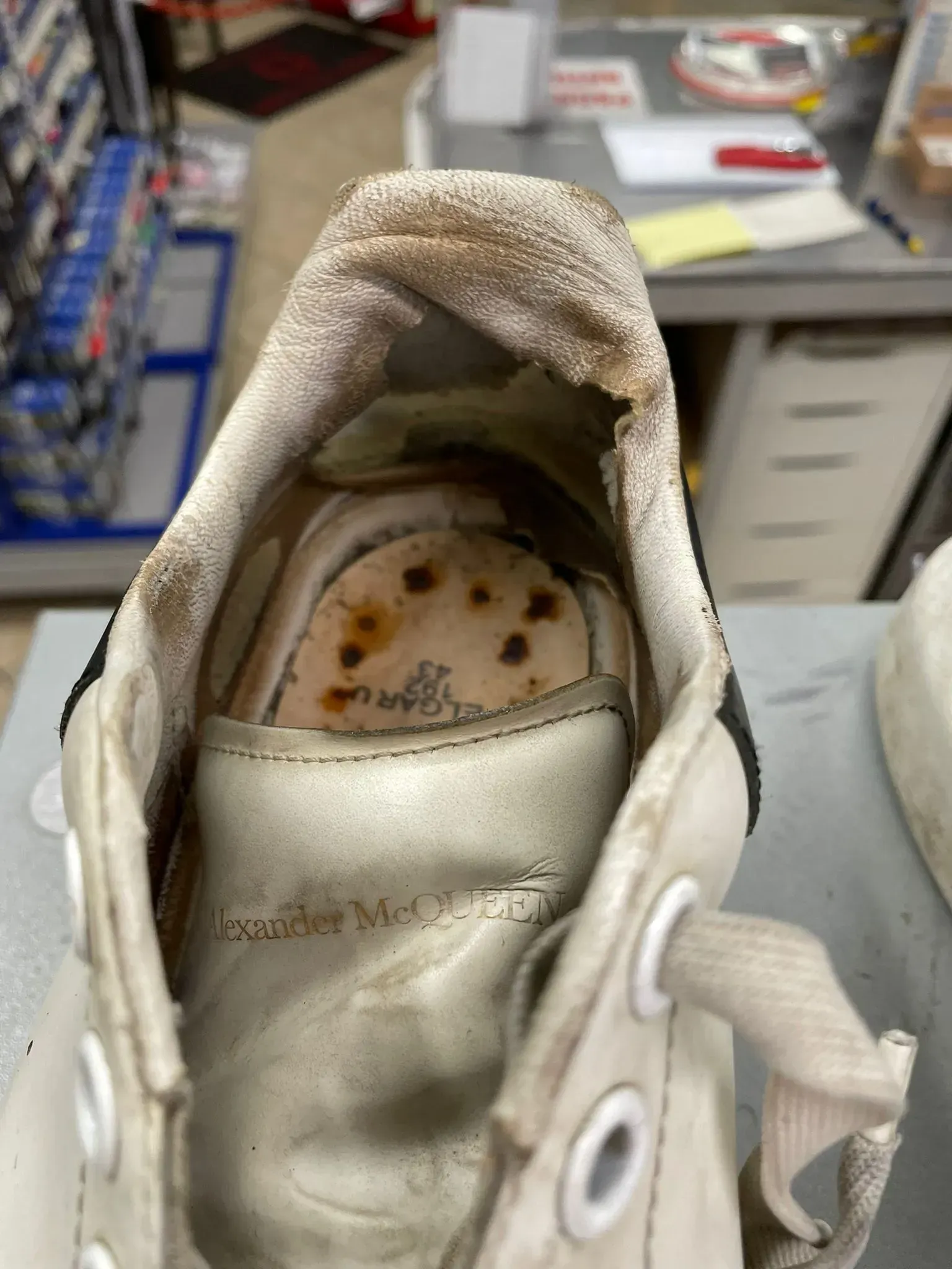 Scarpa da ginnastica sporca con soletta ammuffita e macchiata, mostrata in un'officina o in un magazzino.
