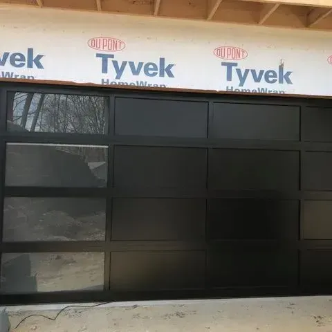 Black-framed glass garage door installed in a construction opening under Tyvek house wrap.
