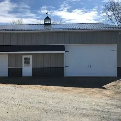 Gray metal building with a white garage door and small entrance door under a blue sky