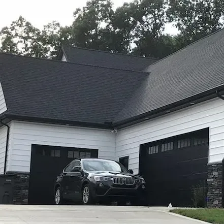 Black SUV parked in front of a white house with a dark roof and black garage doors.