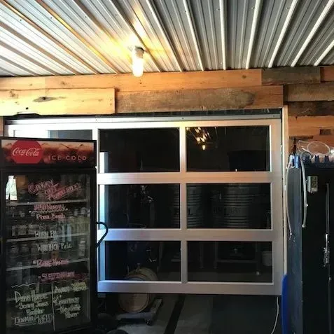Small storefront window under a corrugated metal roof, with a Coca-Cola fridge and hanging clothes inside.