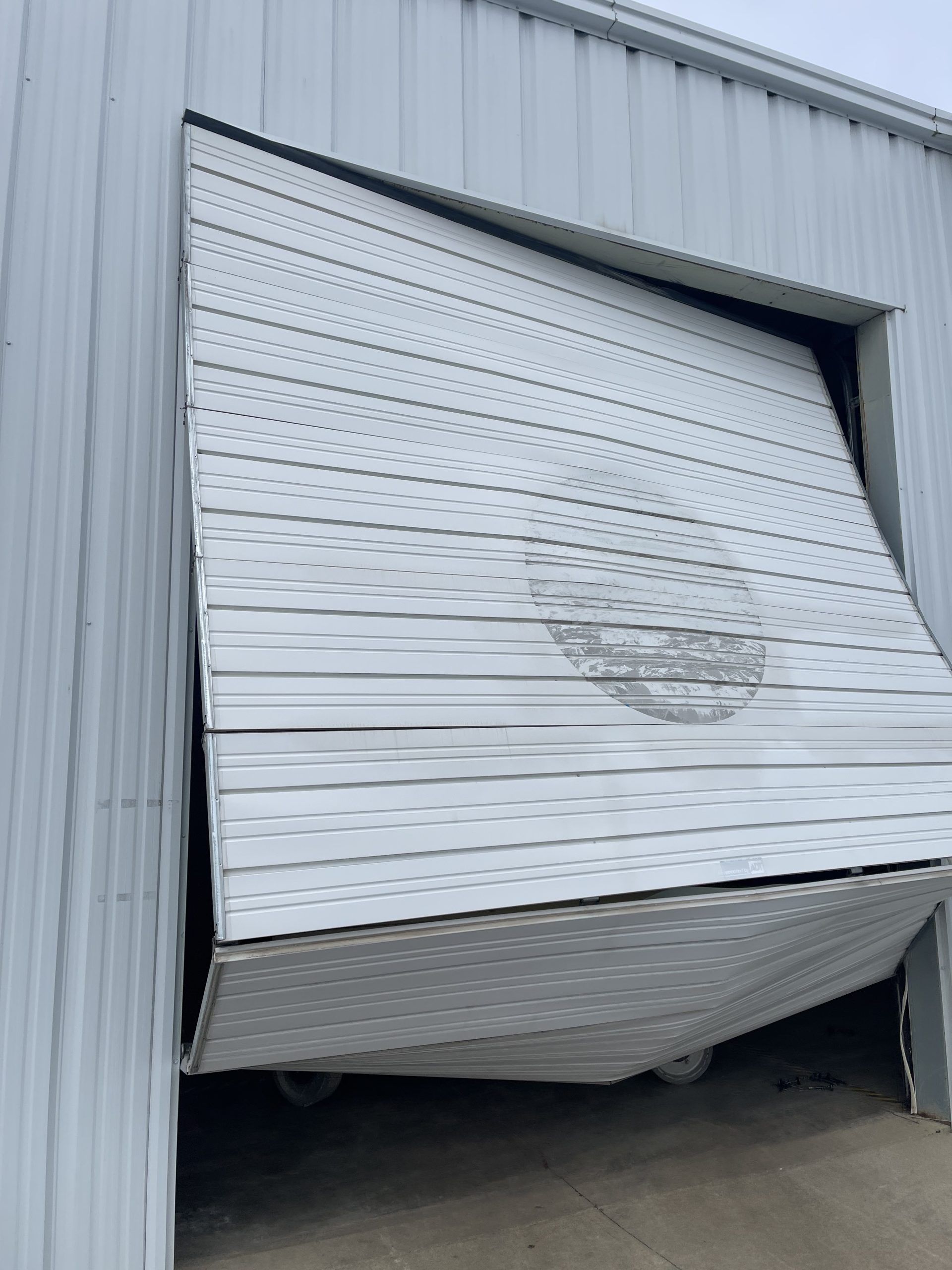 Damaged rolling garage door bent outward on a gray industrial building
