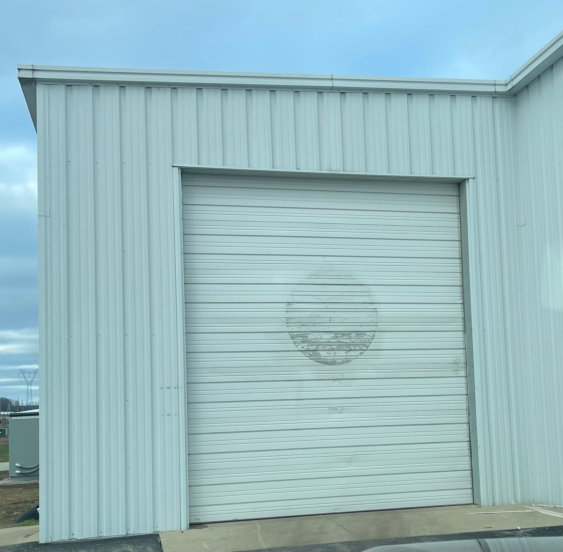 White metal roll-up garage door on a light blue industrial building under a cloudy sky