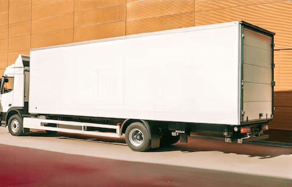 White box truck parked beside a tan wall on a sunlit street