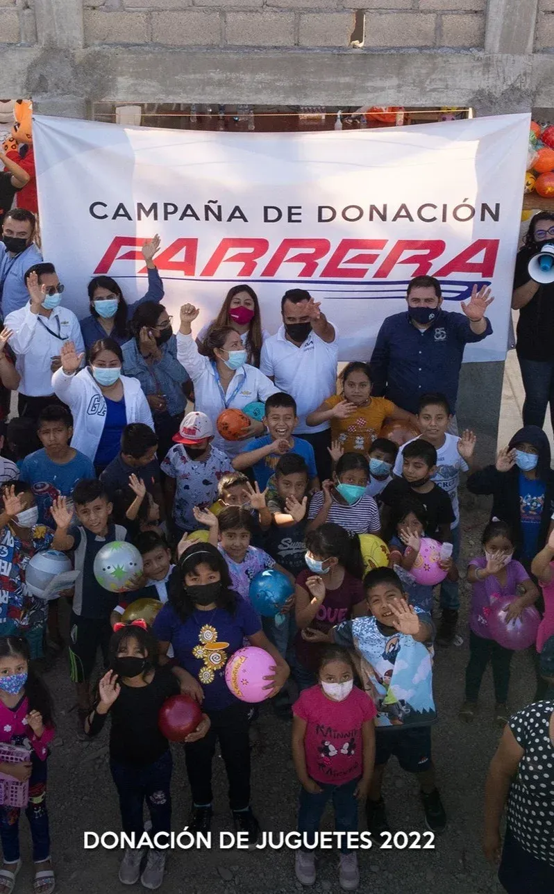 Grupo en campaña de donación de juguetes 2022 frente a un cartel de Barrera, con globos y cajas.