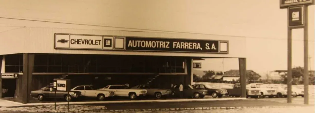 Fotografía antigua en tono sepia de un concesionario de coches Renault con vehículos aparcados bajo una marquesina.