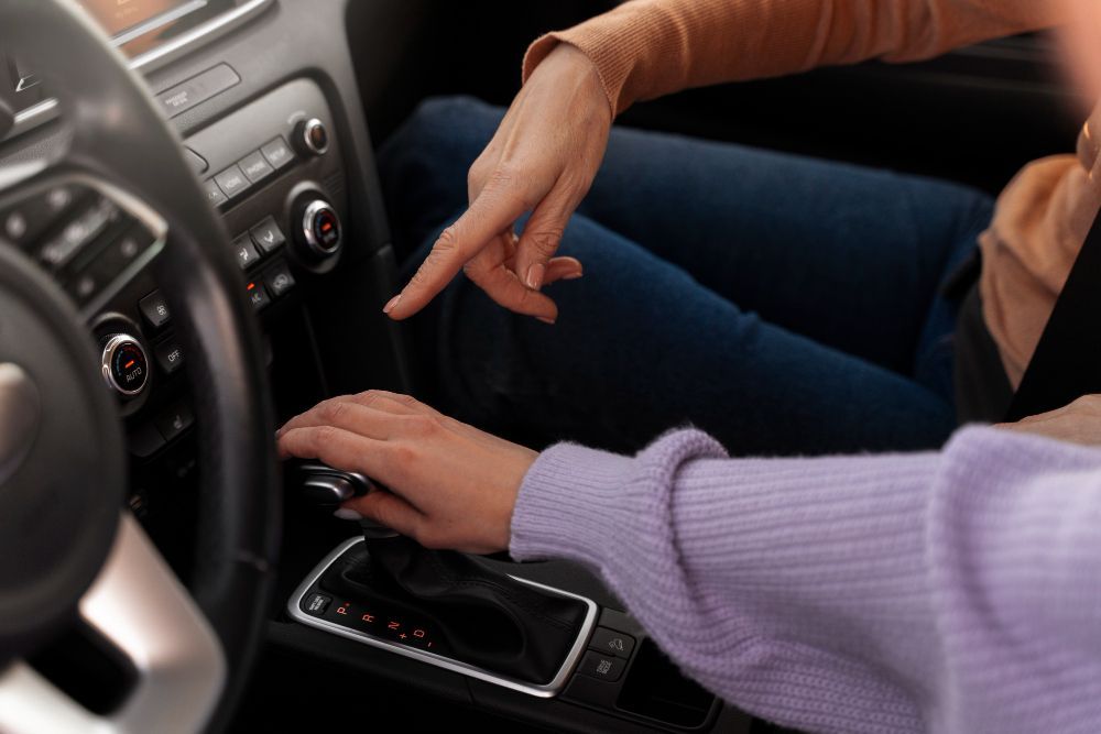 Manos que se extienden hacia la consola central del coche y la palanca de cambios situada en el asiento delantero.
