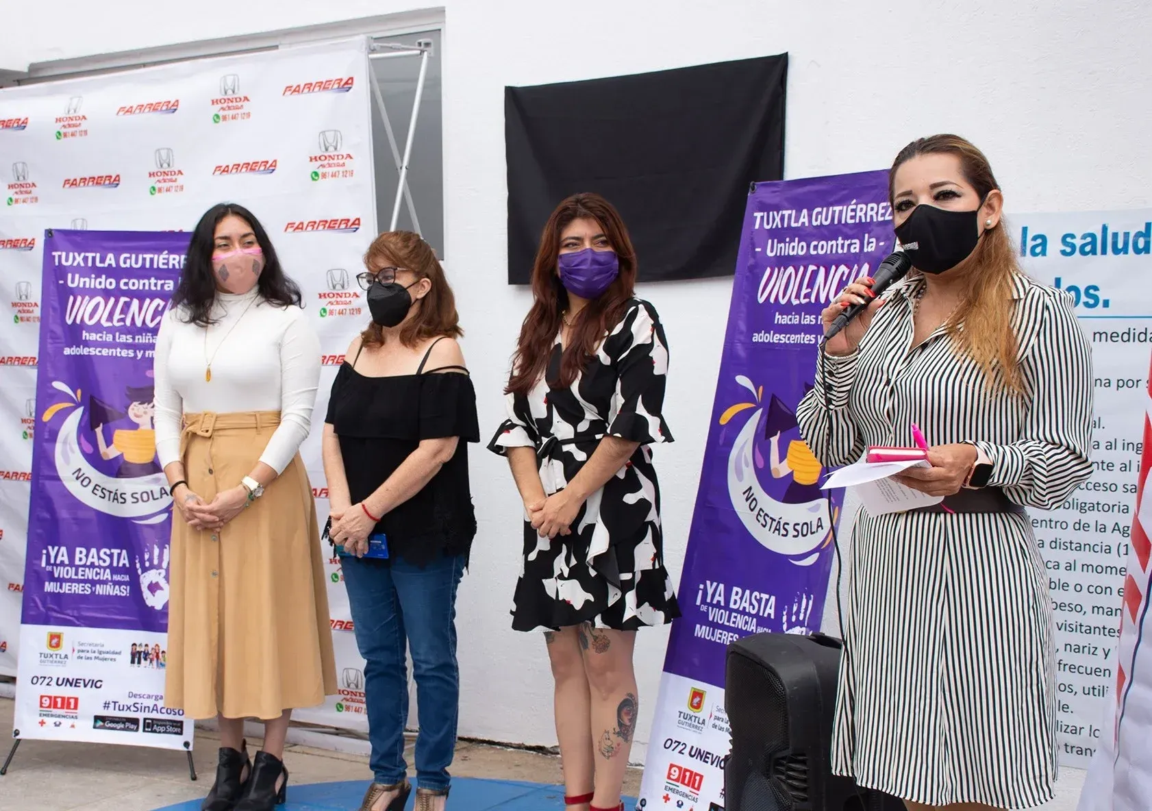 Cuatro personas con mascarillas faciales permanecen de pie en el escenario junto a pancartas moradas del evento.