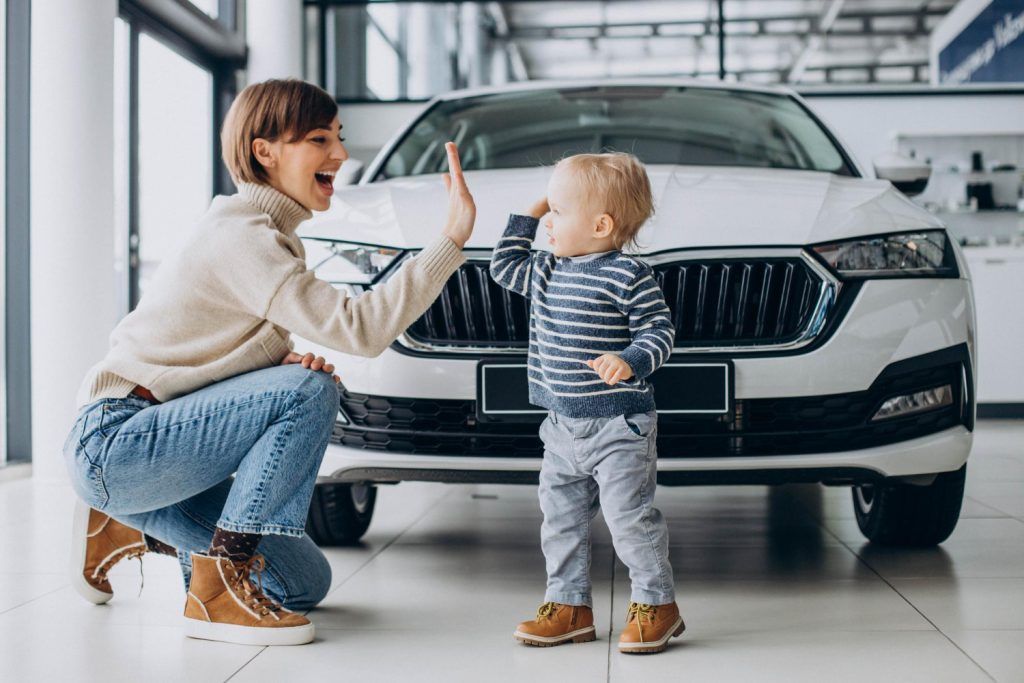 Una mujer arrodillada junto a un niño pequeño frente a un coche blanco