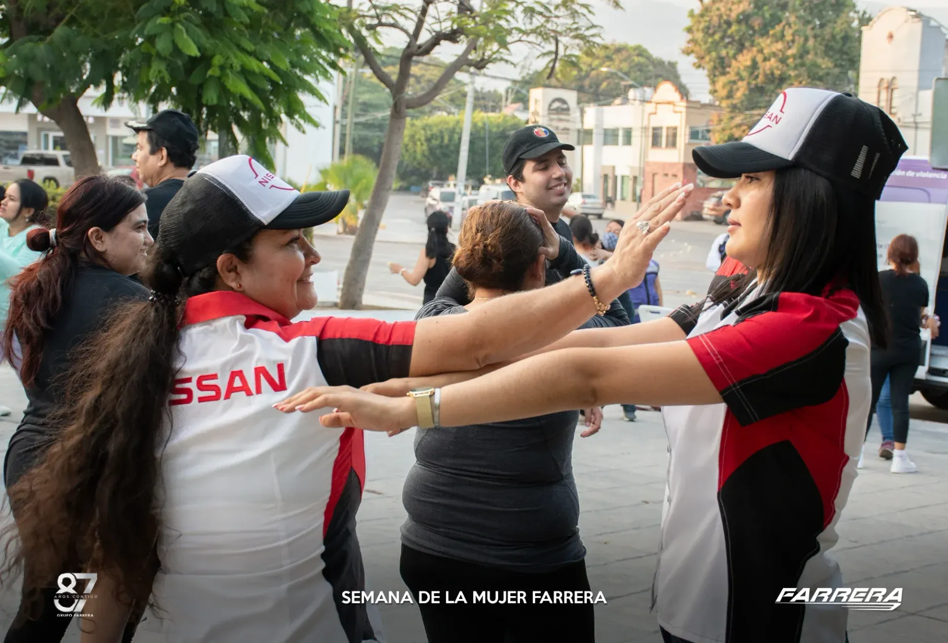 Personas con camisetas deportivas rojas y negras chocan las manos al aire libre en un parque o evento.