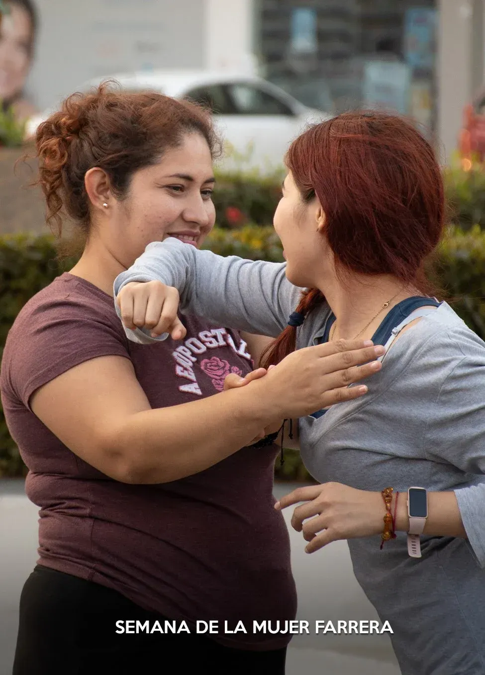 Dos mujeres se abrazan y sonríen en un evento al aire libre, con el texto “Semana de la Mujer Ferrera” en la parte inferior.