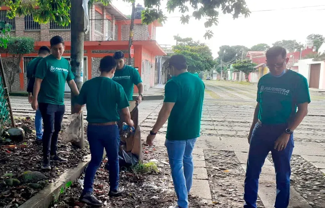 Personas con camisetas verdes caminan por una calle arbolada junto a edificios y motocicletas estacionadas.
