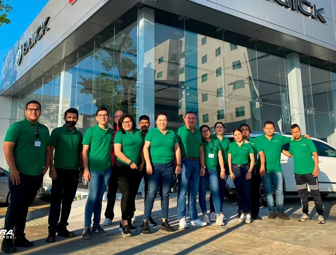 Grupo de personas con camisetas verdes de pie frente a un moderno edificio de oficinas de cristal.