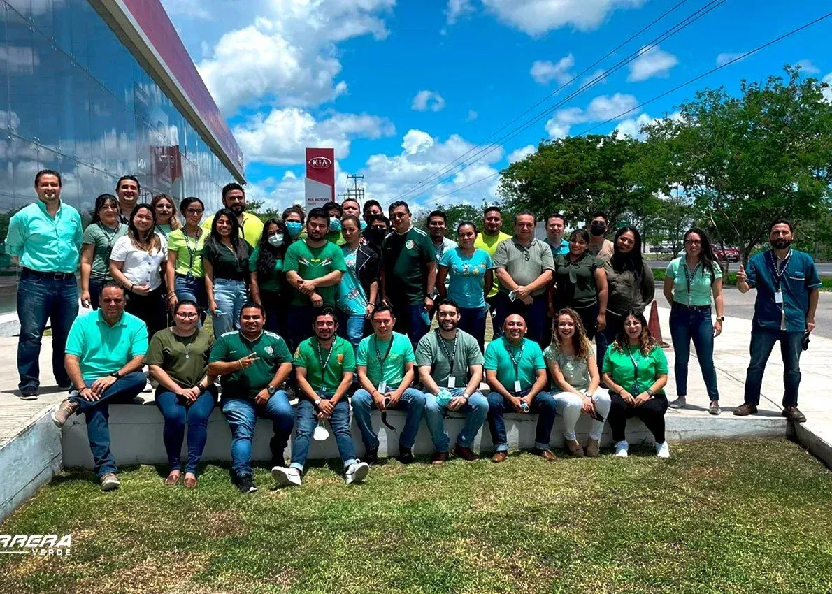 Grupo de personas con camisetas verdes posando al aire libre junto a un edificio bajo un cielo azul.