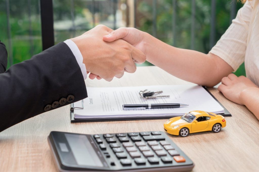 Un apretón de manos sobre los papeles del préstamo del coche con una calculadora y un coche de juguete sobre un escritorio.